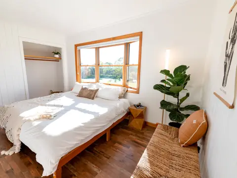 A bright, tidy bedroom with a window, white linen and a plant