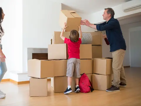 A family stacking cardboard boxes in a bright, empty room