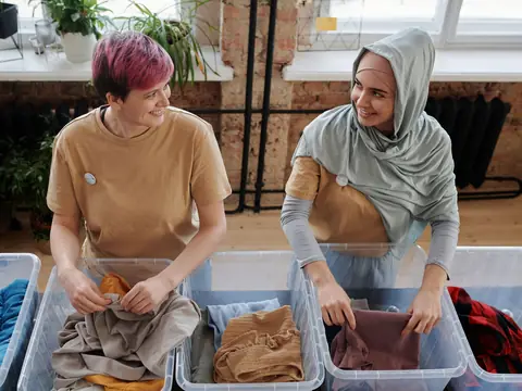 Two smiling women sorting clothes into boxes in a bright room